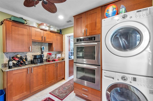 3898 49th Ave S, Saint Petersburg, FL 33711 - kitchen featuring stainless steel double oven, stacked washing machine and dryer, crown molding, brown cabinetry, and a ceiling fan