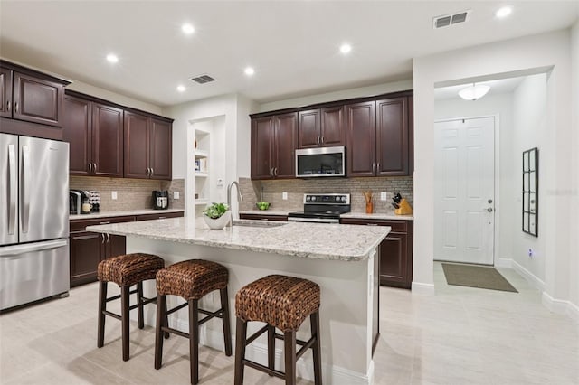 5808 Grand Sonata Ave, Lutz, FL 33558 - kitchen featuring stainless steel appliances, a breakfast bar area, decorative backsplash, dark brown cabinetry, and an island with sink