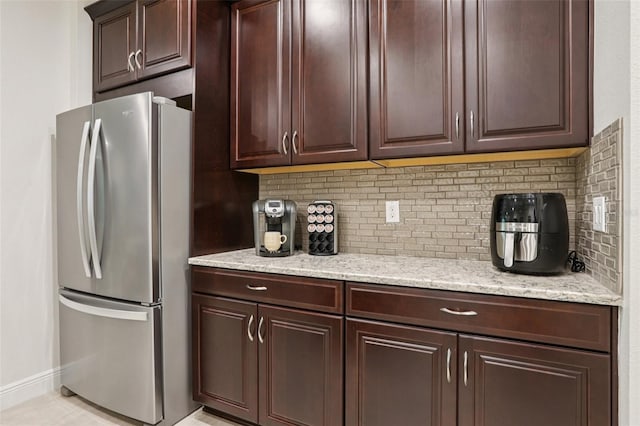 5808 Grand Sonata Ave, Lutz, FL 33558 - kitchen featuring freestanding refrigerator, dark brown cabinetry, decorative backsplash, and light stone counters
