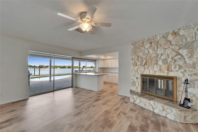 6334 Cocoa Ln, Apollo Beach, FL 33572 - unfurnished living room with light wood-style floors, a water view, a ceiling fan, a stone fireplace, and a textured ceiling