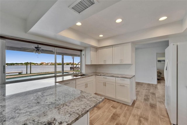 6334 Cocoa Ln, Apollo Beach, FL 33572 - kitchen featuring white appliances, a tray ceiling, light wood-style floors, white cabinetry, and light stone counters