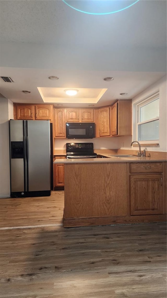 7107 Hernando Ct, Tampa, FL 33615 - kitchen featuring black appliances, a raised ceiling, wood finished floors, light countertops, and a peninsula