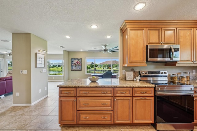 2110 W View Dr, Sun City Center, FL 33573 - kitchen featuring appliances with stainless steel finishes, a ceiling fan, light stone countertops, brown cabinetry, and a textured ceiling