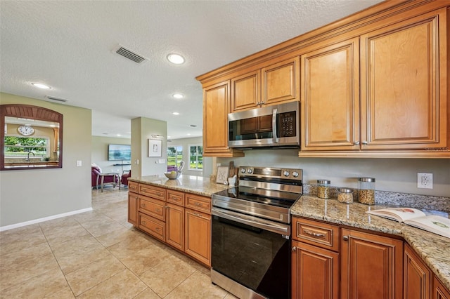2110 W View Dr, Sun City Center, FL 33573 - kitchen featuring stainless steel appliances, light tile patterned floors, brown cabinets, light stone counters, and a textured ceiling