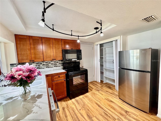 3902 Glissade Dr, New Port Richey, FL 34652 - kitchen featuring black appliances, light wood-type flooring, brown cabinets, tasteful backsplash, and a tray ceiling