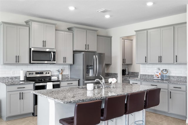 33675 Elm Hill Br, Wesley Chapel, FL 33545 - kitchen featuring appliances with stainless steel finishes, gray cabinets, light stone counters, a kitchen breakfast bar, and recessed lighting