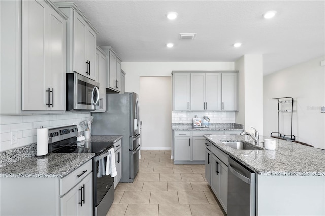 33675 Elm Hill Br, Wesley Chapel, FL 33545 - kitchen featuring appliances with stainless steel finishes, decorative backsplash, a center island with sink, gray cabinetry, and light stone countertops
