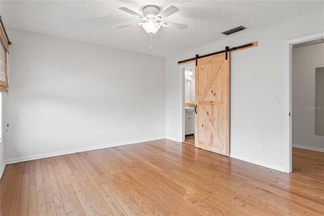 15636 Morning Dr, Lutz, FL 33559 - unfurnished bedroom featuring a barn door, light wood finished floors, a textured ceiling, connected bathroom, and ceiling fan