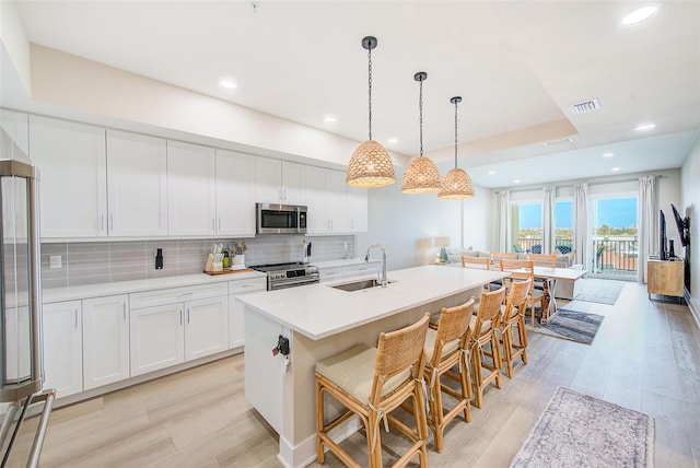 400 150th Ave Unit 504, Madeira Beach, FL 33708 - kitchen featuring appliances with stainless steel finishes, light wood-style floors, tasteful backsplash, white cabinets, and an island with sink