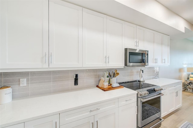 400 150th Ave Unit 504, Madeira Beach, FL 33708 - kitchen featuring appliances with stainless steel finishes, white cabinetry, tasteful backsplash, light wood finished floors, and light countertops
