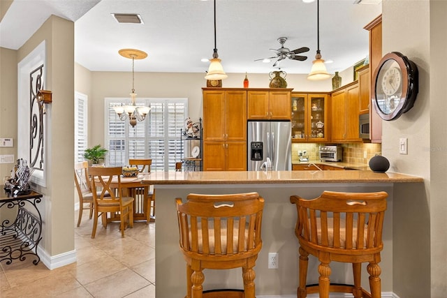 15744 Crystal Waters Dr, Wimauma, FL 33598 - kitchen featuring stainless steel appliances, brown cabinets, ceiling fan, glass insert cabinets, and tasteful backsplash