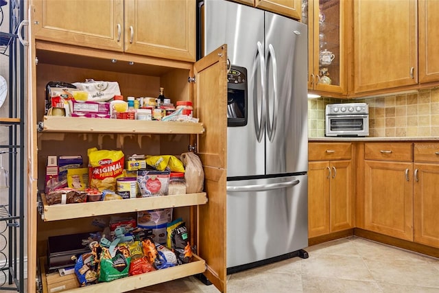 15744 Crystal Waters Dr, Wimauma, FL 33598 - kitchen with stainless steel fridge, decorative backsplash, brown cabinetry, glass insert cabinets, and light tile patterned floors