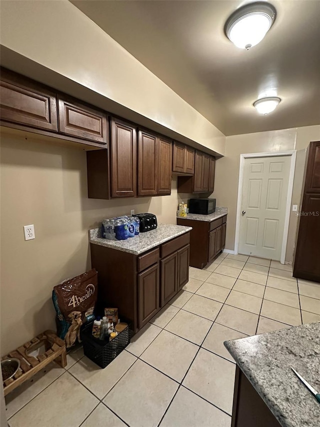 120 Henry St, Interlachen, FL 32148 - kitchen with black microwave, light tile patterned floors, dark brown cabinetry, and light stone countertops