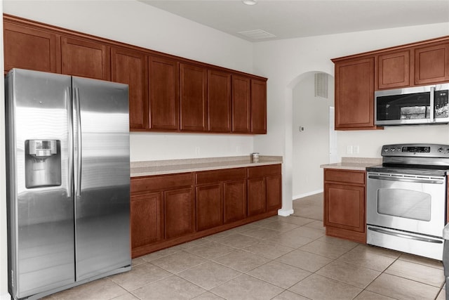 1280 Hill Flower Dr, Brooksville, FL 34604 - kitchen featuring appliances with stainless steel finishes, arched walkways, light countertops, light tile patterned floors, and brown cabinetry