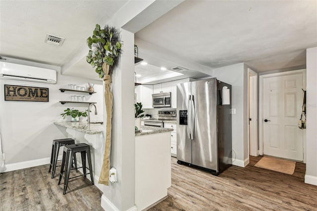 5744 Thrush Dr, New Port Richey, FL 34652 - kitchen with stainless steel appliances, a wall unit AC, light wood-style flooring, white cabinetry, and recessed lighting