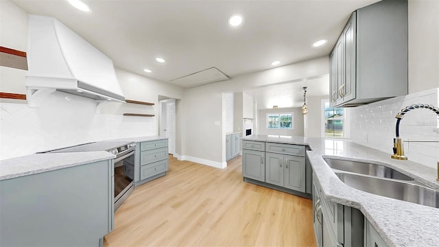 1005 45th St W, Bradenton, FL 34209 - kitchen with gray cabinets, stainless steel range with electric stovetop, light wood-style floors, premium range hood, and decorative backsplash