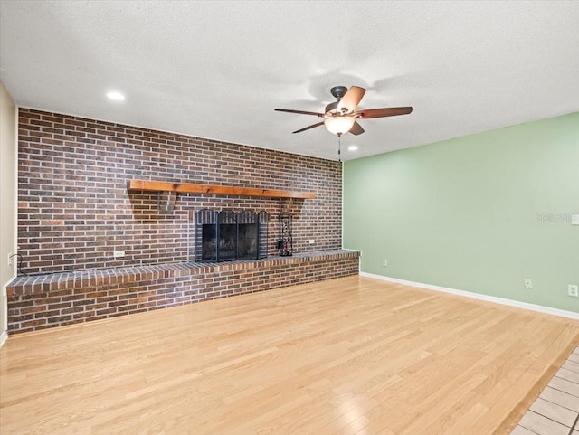 1015 Hastings Ct, Lutz, FL 33548 - unfurnished living room featuring ceiling fan, wood finished floors, a textured ceiling, a fireplace, and brick wall