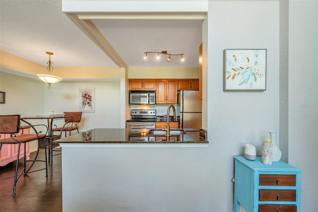 3301 Haviland Ct Unit 301, Palm Harbor, FL 34684 - kitchen featuring stainless steel appliances, a peninsula, brown cabinetry, hanging light fixtures, and dark wood-type flooring