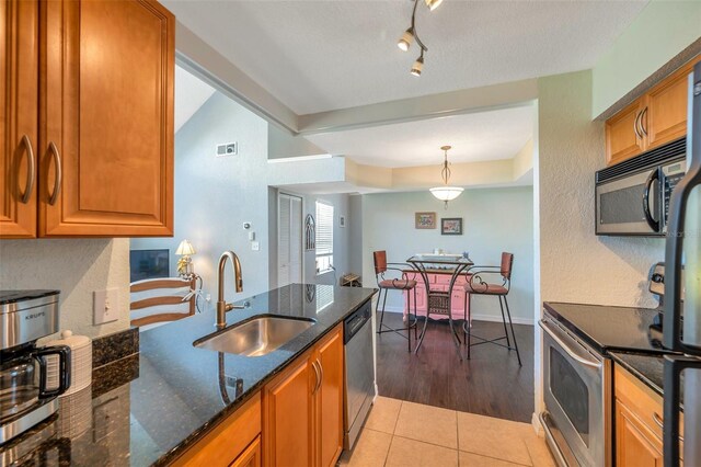 3301 Haviland Ct Unit 301, Palm Harbor, FL 34684 - kitchen with appliances with stainless steel finishes, dark stone counters, brown cabinetry, light tile patterned floors, and a textured wall