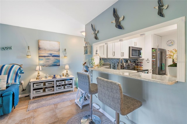 5725 Pelican Pointe Dr Unit 1, Sebastian, FL 32958 - kitchen featuring appliances with stainless steel finishes, white cabinets, backsplash, a kitchen bar, and light stone counters