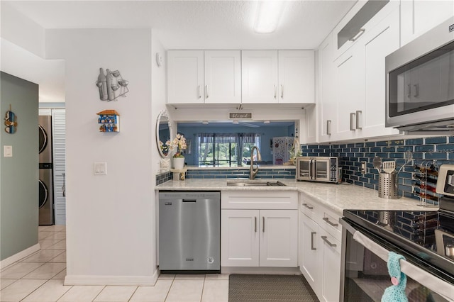 5725 Pelican Pointe Dr Unit 1, Sebastian, FL 32958 - kitchen featuring stainless steel appliances, stacked washer and clothes dryer, tasteful backsplash, light tile patterned flooring, and white cabinetry