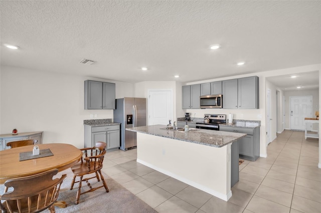 7774 Sail Clover Ln, Zephyrhills, FL 33540 - kitchen with appliances with stainless steel finishes, gray cabinets, light tile patterned flooring, light stone counters, and a kitchen island with sink