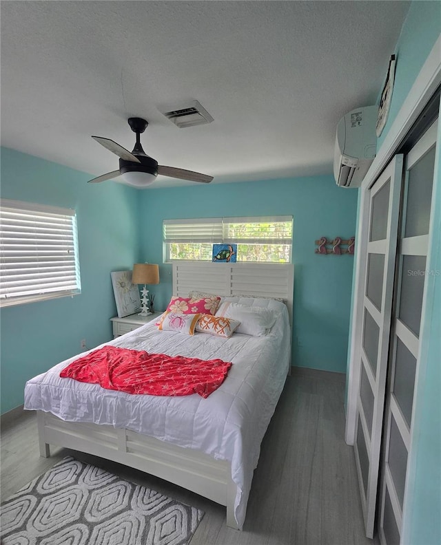 1626 Sea Breeze Dr, Tarpon Springs, FL 34689 - bedroom featuring wood finished floors, a wall mounted air conditioner, ceiling fan, and a textured ceiling