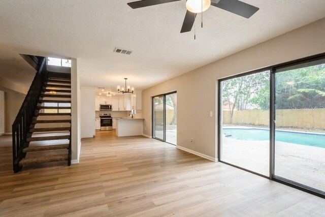 14909 Oldgate Pl, Tampa, FL 33624 - unfurnished living room with stairway, light wood-style flooring, a chandelier, a ceiling fan, and a textured ceiling