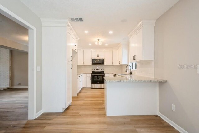 14909 Oldgate Pl, Tampa, FL 33624 - kitchen with appliances with stainless steel finishes, a peninsula, light stone counters, light wood-style floors, and white cabinetry