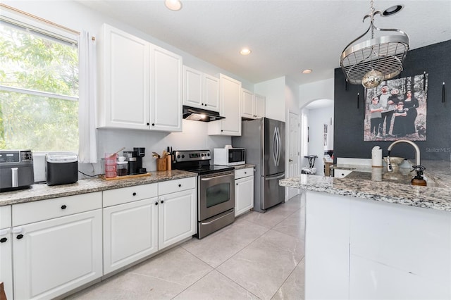 8050 Diablo Ct, Trinity, FL 34655 - kitchen featuring stainless steel appliances, under cabinet range hood, arched walkways, light tile patterned floors, and white cabinetry