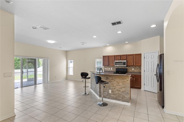 12631 Chenwood Ave, Hudson, FL 34669 - kitchen with black appliances, a kitchen bar, open floor plan, light tile patterned floors, and decorative backsplash