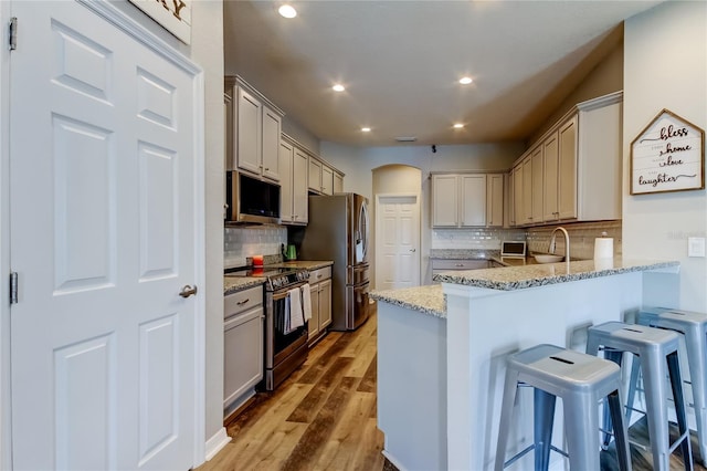 6648 Castle Green Pl, Zephyrhills, FL 33541 - kitchen with appliances with stainless steel finishes, arched walkways, a peninsula, a kitchen bar, and backsplash