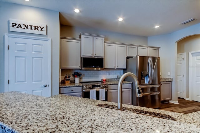 6648 Castle Green Pl, Zephyrhills, FL 33541 - kitchen featuring appliances with stainless steel finishes, dark wood finished floors, arched walkways, recessed lighting, and backsplash