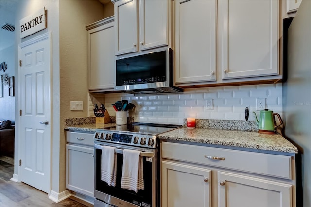 6648 Castle Green Pl, Zephyrhills, FL 33541 - kitchen with stainless steel appliances, tasteful backsplash, light wood-style floors, and light stone countertops