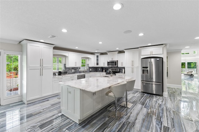 3663 Berger Rd, Lutz, FL 33548 - kitchen featuring appliances with stainless steel finishes, white cabinets, recessed lighting, backsplash, and an island with sink