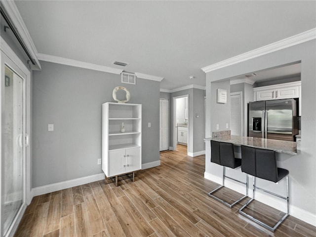 13285 Arbor Pointe Cir Unit 202, Tampa, FL 33617 - kitchen with stainless steel fridge, wood finished floors, white cabinets, crown molding, and a kitchen breakfast bar