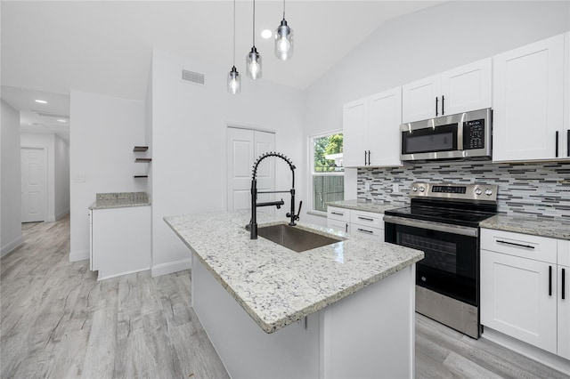 2859 38th Ave N, Saint Petersburg, FL 33713 - kitchen with appliances with stainless steel finishes, light wood-style floors, an island with sink, white cabinets, and tasteful backsplash