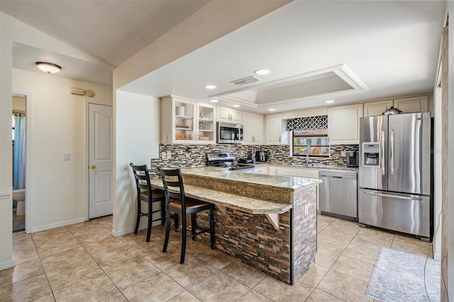 37147 Foxrun Pl, Zephyrhills, FL 33542 - kitchen with stainless steel appliances, decorative backsplash, a peninsula, a raised ceiling, and a kitchen bar