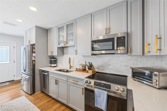 4521 S Cooper Pl, Tampa, FL 33611 - kitchen featuring stainless steel appliances, gray cabinets, decorative backsplash, light wood-type flooring, and glass insert cabinets