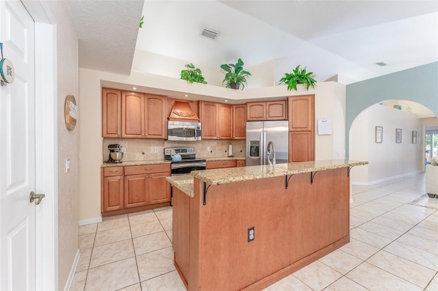 835 Symphony Isles Blvd, Apollo Beach, FL 33572 - kitchen featuring appliances with stainless steel finishes, light tile patterned flooring, a breakfast bar area, light stone countertops, and vaulted ceiling