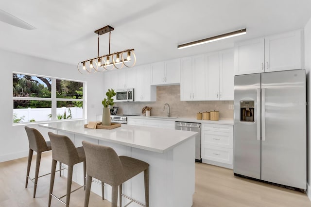 3381 19th Pl SW, Largo, FL 33774 - kitchen with appliances with stainless steel finishes, light wood-type flooring, decorative backsplash, white cabinetry, and a center island