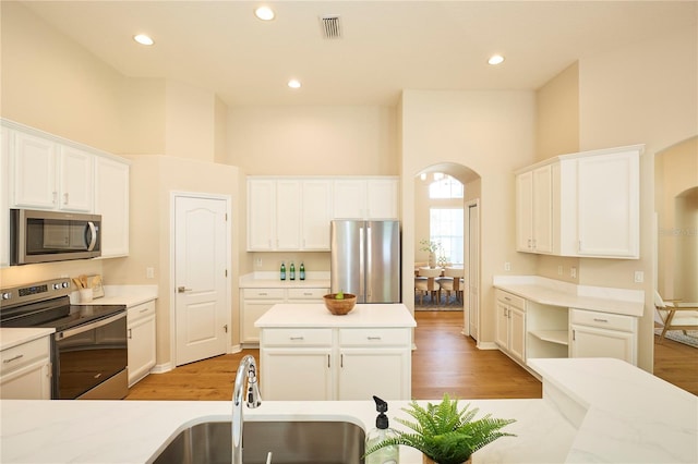 15412 Carrillon Estates Blvd, Tampa, FL 33625 - kitchen with stainless steel appliances, arched walkways, light wood-style flooring, white cabinets, and a high ceiling