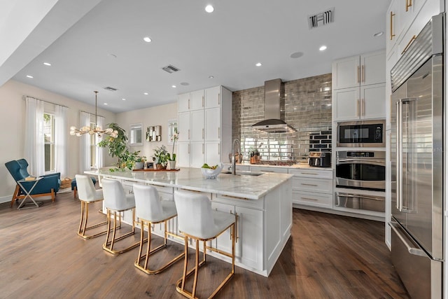 2711 W Trilby Ave, Tampa, FL 33611 - kitchen featuring built in appliances, wall chimney exhaust hood, a warming drawer, white cabinets, and dark wood finished floors