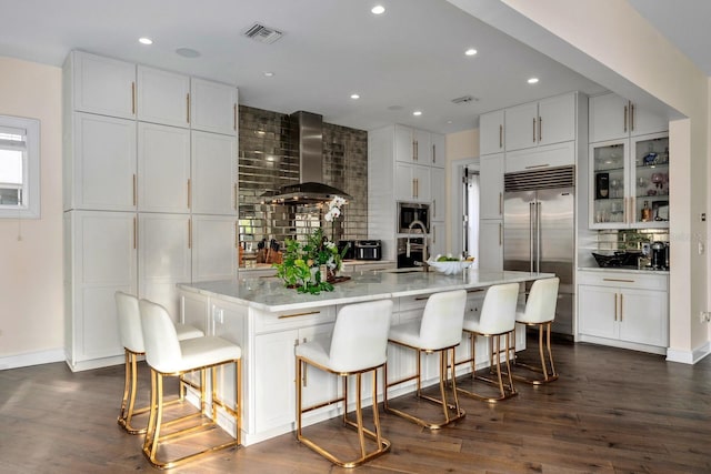 2711 W Trilby Ave, Tampa, FL 33611 - kitchen with wall chimney exhaust hood, built in appliances, decorative backsplash, white cabinetry, and dark wood-style floors
