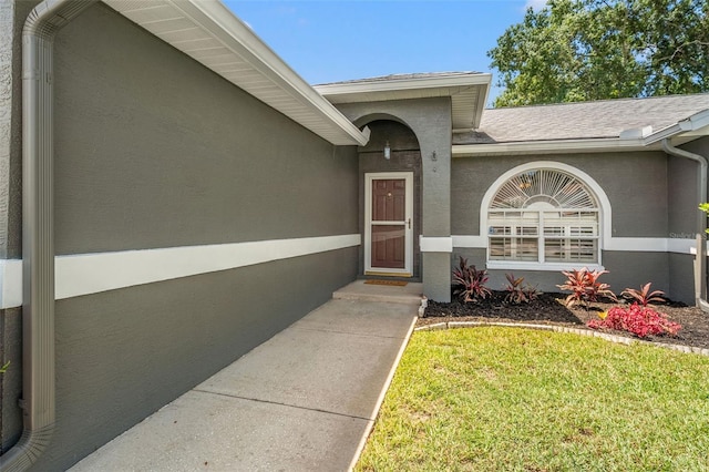 10032 Basin St, New Port Richey, FL 34655 - doorway to property featuring a lawn, stucco siding, and roof with shingles