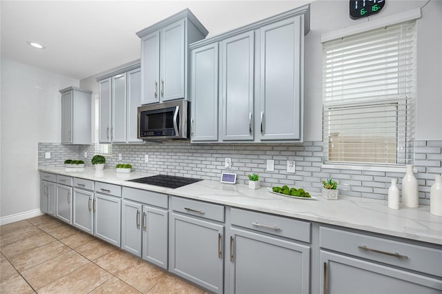 1601 Fox Grape Loop, Lutz, FL 33558 - kitchen featuring stainless steel microwave, gray cabinetry, black electric cooktop, light tile patterned flooring, and backsplash
