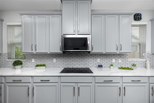 1601 Fox Grape Loop, Lutz, FL 33558 - kitchen featuring stainless steel microwave, black electric cooktop, decorative backsplash, gray cabinets, and light stone counters