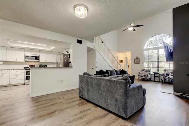 7320 Hideaway Trl, New Port Richey, FL 34655 - living room featuring stairs, a textured ceiling, light wood-style floors, ceiling fan, and a towering ceiling