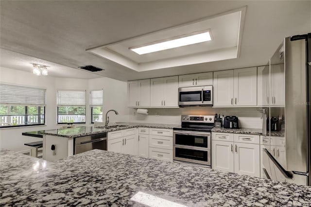 7320 Hideaway Trl, New Port Richey, FL 34655 - kitchen with appliances with stainless steel finishes, a peninsula, white cabinets, a tray ceiling, and stone counters