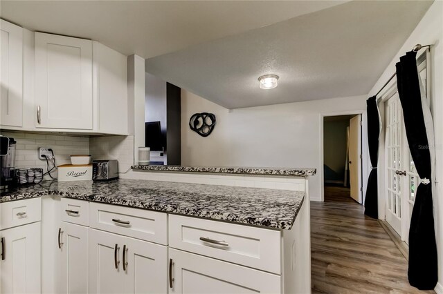 7320 Hideaway Trl, New Port Richey, FL 34655 - kitchen featuring a peninsula, dark stone countertops, white cabinets, tasteful backsplash, and wood finished floors